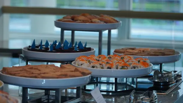 Açık büfe tepsilerinde servis edilen suşi, çikolatalı kek, ekmek ve sandviçler de dahil olmak üzere çeşitli uluslararası yemekler..