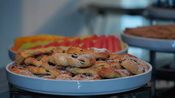 Beyaz bir tabakta servis edilen pudra şekerli çikolatalı pastalar, arka planda taze meyveler, kahvaltı ya da tatlı için büfe masasında sergileniyor..