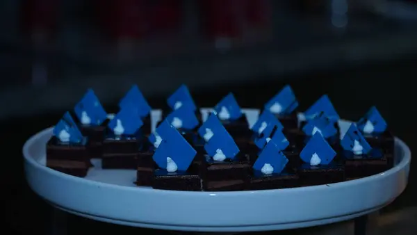 Üzerinde canlı mavi çikolata parçaları ve krema noktaları olan mini çikolatalı kremalı kekler beyaz seramik tepside zarif bir şekilde sunuluyor. Lüks tatlı ya da yemek servisi için ideal..