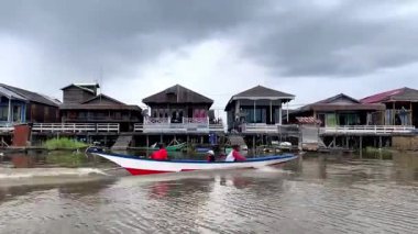 Kartanegara, Doğu Kalimantan, Endonezya - 15 Ağustos 2024: Geleneksel ahşap evler Melintang Gölü kıyısında huzurlu bir köy ortamında günlük kırsal yaşamı su kenarında gösteriyor.