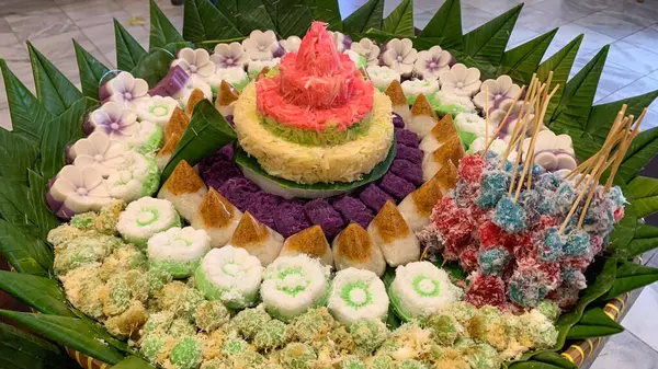 Muz yaprakları üzerinde renkli Endonezya geleneksel aperatifleri, katmanlı pirinç kekleri ve hindistan cevizi tatlılarının yer aldığı festival ve kültürel bir sunum.