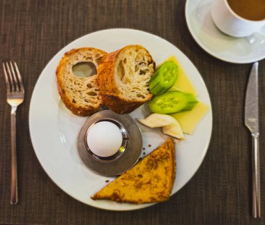 Beyaz tabakta yumurta, ekmek, peynir ve sebzeli basit Avrupa kahvaltısı