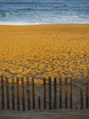 Ahşap çit, gün batımında kumlu sahilde gölgeler bırakıyor.
