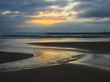 Altın gün batımı yansıması okyanus dalgaları ve dramatik gökyüzü ile ıslak kum üzerinde