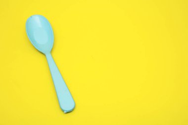 Sarı arka planda tek bir mavi plastik kaşık.