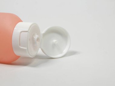 Pastel turuncu veya şeftali tonlu plastik bir tüpte açık duran beyaz bir kapağın ayrıntılı görüntüsü. Basit tasarım cilt bakımı, kozmetik veya kişisel bakım için kullanıcı dostu bir ürün önerir.