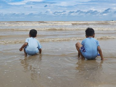 İki çocuk denizin sahilinde oturuyor.