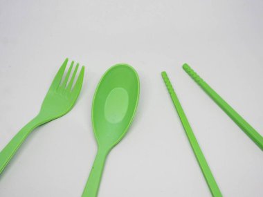 Temiz beyaz arka planda parlak yeşil tek kullanımlık plastik çatal bıçak seti. Bir çatal, kaşık ve yemek çubuğu içerir, genellikle yemek servislerinde, pikniklerde ya da tek kullanımlık aletlerin tercih edildiği etkinliklerde kullanılır..