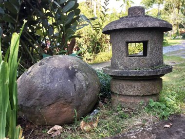 Yıpranmış taştan bir fener ve kayalık verimli bir bahçede geleneksel Asya bahçe tasarımı ve huzurlu doğal güzelliği çağrıştırıyor..
