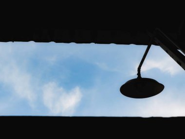 Açık hava lambasının çarpıcı bir silueti bulutlu yumuşak mavi gökyüzüne karşı minimalist ve sakin bir sahne yaratıyor..