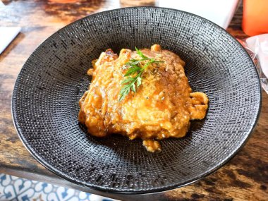 Lezzetli ev yapımı lazanya, altın rengi erimiş peynir ve siyah tabakta taze maydanoz. Zengin ve rahatlatıcı bir İtalyan yemeği..