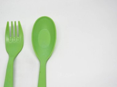 Temiz beyaz arka planda parlak yeşil plastik çatal ve kaşık. Yemek temaları, çevre dostu ürünler, partiler veya çocukla ilgili içerik için ideal.