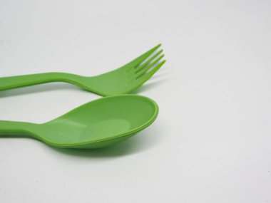 Canlı yeşil plastik çatal ve kaşık, temiz beyaz arka planda hafifçe açılı. Yemek, piknik, çevre dostu ya da çocuk yemek temaları için mükemmel..