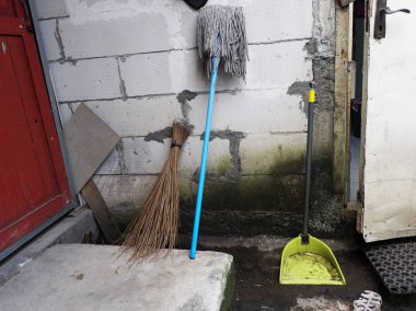 Eski, dokulu bir duvara dayanan süpürge, süpürge, paspas ve faraş gibi sıradan temizlik aletleri koleksiyonu. Ev işleri teması için mükemmel..