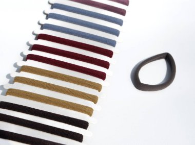 Çapraz bir sıra halinde ambalajlarında çeşitli renkli saç bağları sergilenir, tek bir kahverengi saç teli temiz beyaz arka planda yanlarına bir döngü olarak yerleştirilir..