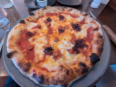 Çeşitli malzemelerle nefis bir pizza yenmeye hazır bir tabakta oturur. Kabuğu güzelce kahverengileşmiş..