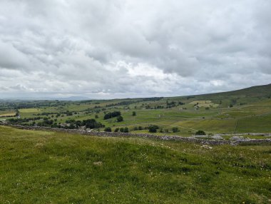 Kırsal bir manzara bulutlu bir gökyüzünün altında, yuvarlanan tepeler ve taş duvarlarla.