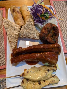 Enfes bir tabakta çeşitli Asya aperatifleri sergileniyor. İçinde börek, susamlı tost, pirzola ve tavuk şişleri var. Hepsi de güzelce yerleştirilmiş..
