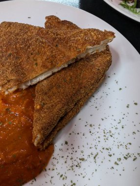 Beyaz bir tabakta canlı domates sosuyla servis edilen ve yenmeye hazır kızarmış bir tabağın yakın çekimi..