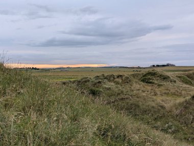 Güneşin battığı uzak bir şatonun silueti ile yuvarlanan yeşil tarlaların üzerinde güzel bir akşam gökyüzünü yakalıyor..