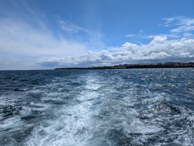 Güzel, bulutlu bir gökyüzünün altında, sahilin arka planına karşı okyanusun uyanışını gösteren manzaralı bir tekne manzarası..