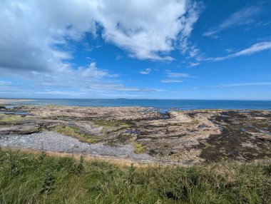 Çarpıcı bir kıyı manzarası bulutlarla benekli parlak mavi bir gökyüzü ile doğanın dingin güzelliğini gözler önüne seriyor..