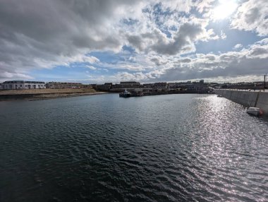 Limanın sakin suları bulutlu gökyüzünü yansıtır. Parlak bir günde binalar ve bir tekne görünür..