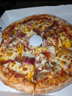 Lezzetli, taze pişmiş bir pizza kutusunda, tadını çıkarmaya hazır, çeşitli malzemelerle birlikte renkli bir görüntü oluşturur..