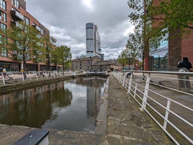 Modern bir şehirde manzaralı bir kanal. Bulutlu bir gökyüzünün altında su kenarında binalar ve ağaçlar var..