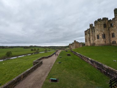 Northumberland, İngiltere 'deki Alnwick Kalesi' nin manzarası bulutlu bir günde insanların yol boyunca yürüdüğü yeşil bir manzara..