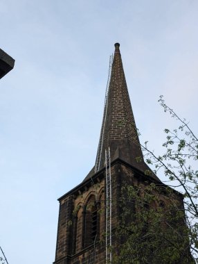 Yukarıya bakan bir perspektif, merdivenlerle süslenmiş bir kilise kulesini yakalar. En üstte, sakin bir gökyüzünün altında bakım ve onarım çalışmaları yapılmasını önerir..