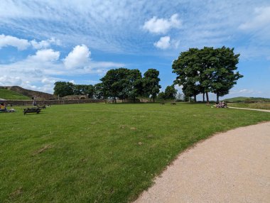 Bereketli yeşillik, ağaçlar ve bulutlu açık mavi bir gökyüzü içeren manzaralı bir çekim. İnsanlar arka planda dinleniyor. Fotoğrafta bir patika da var..