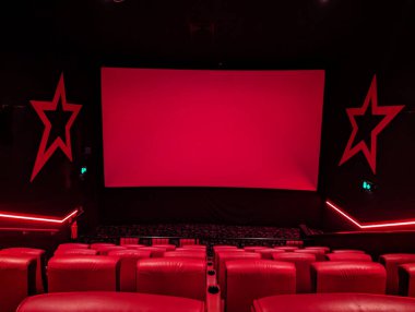 Kırmızı koltuklu ve büyük ekranlı bir sinema manzarası, kırmızı ışıkla aydınlatılmış, film deneyimi için hazır..