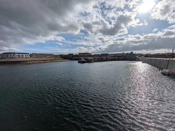 Limanın sakin suları bulutlu gökyüzünü yansıtır. Parlak bir günde binalar ve bir tekne görünür..