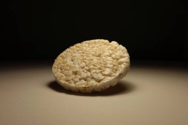 Tarafsız bir arkaplanda dramatik ışıklandırmada pofuduk pirinç kekinin minimalist fotoğrafı. Temiz ve basit kompozisyon, sağlıklı yiyecekler, atıştırmalıklar ya da modern diyet kavramları için mükemmel.