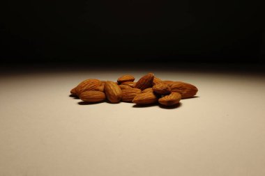 Huysuz ışıkların altında bej bir yüzeye yerleştirilmiş doğal bademler. Yumuşak gölgeli minimalist kompozisyon. Sağlıklı beslenme, vegan atıştırmalıkları veya organik yaşam tarzı görselleri için ideal.