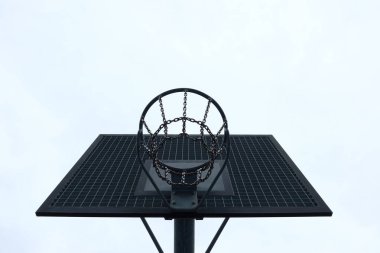 Metal bir zincir ağ ve kapalı bir gökyüzüne karşı ızgara sehpası olan basketbol çemberinin altından bak. Şehir tarzı minimalizm, oyuncuların sahadaki perspektifinden çekilmiştir.
