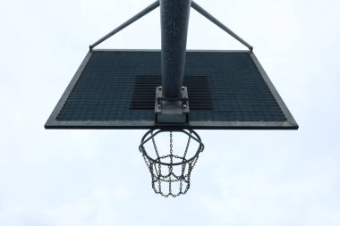 Zincir ağlı metal bir basketbol potası ve parlak bir gökyüzüne karşı siyah bir sedye. Şehir dışı sporları endüstriyel mahkeme ekipmanları ve minimalist kompozisyonu gösteriyor.