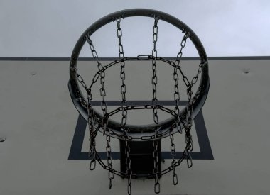 Bulutlu gri gökyüzüne karşı metal zincirli bir basketbol potasının yakın plan görüntüsü. Ağ ve çemberin dış sahadaki yapısını gösteriyor.
