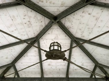 Vintage aydınlatma armatürüne sahip endüstriyel metal tavan yapısı, geometrik çelik kirişler ve yıpranmış beyaz ahşap paneller, aşağıdan çekilen simetrik mimari detay