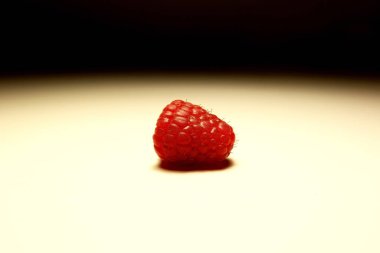 Beyaz arka planda tek olgun ahududu, yumuşak gölgeler ve stüdyo ışıklandırması ile izole edilmiş yakın çekim, makro meyve fotoğrafçılığı, canlı kırmızı renkli minimal gıda konsepti