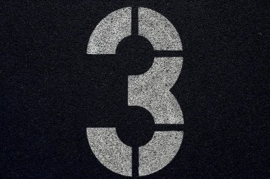 Mavi sentetik koşu pisti yüzeyinde 3 numaralı şerit işaretleme, güneş ışığı altında desenli lastik zemin ve beyaz şablon numarasıyla atletizm pistinin yakın çekim detayları