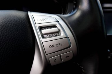 Direksiyon simidine yakın çekim. Seyir kontrolü ve telefon düğmeleri var. Sürücü konforu ve elsiz iletişim için kontrol paneli ile modern araç iç tasarımı