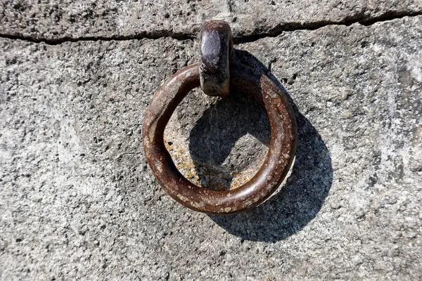 Beton bir göl duvarına sabitlenmiş paslı metal bir demirleme halkasının yakın çekimi, muhtemelen tekneleri bağlamak için kullanılır. Yaş dokusuna ve doğal ışığa sahip denizsel detay, arkaplan veya editoryal kullanım için ideal