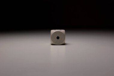 Yumuşak gölgeli ve karamsar ışıklandırmalı pürüzsüz nötr yüzeye odaklanmış tek bir noktayı gösteren tek bir tahta zarın minimalist fotoğrafı
