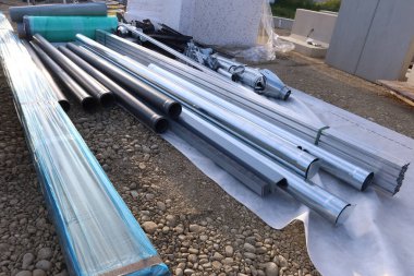 Metal ve plastik borular da dahil olmak üzere çeşitli inşaat boruları ve inşaat malzemeleri, açık hava inşaat sahasında istiflenmiş, kurulum için hazırlanıyor.