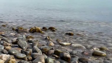 Sakin bir gölün yumuşak dalgaları sakin bir günde kayalık kıyı şeridi boyunca kayalara çarpıyor.