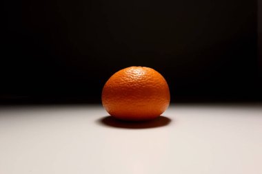 Olgun tek bir mandalinanın minimalist fotoğrafı. Tarafsız arka planda çarpıcı ışıklandırma, sağlıklı turunçgil meyvesi kavramı.