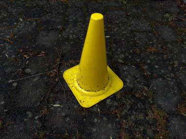 Açık hava spor sahasının koyu ıslak asfalt yüzeyi üzerinde sarı plastik eğitim konisi. Talim, beden eğitimi ya da çocuk oyunları için kullanılır. Kontrastlı ve desenli izole nesne