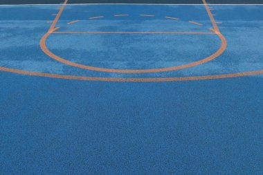 Basketbol işaretli ve ıslak yüzeyi turuncu yarı daireli renkli mavi spor sahasının en üst görüntüsü. Dokuya sahip kentsel atletizm alanı geçmişi